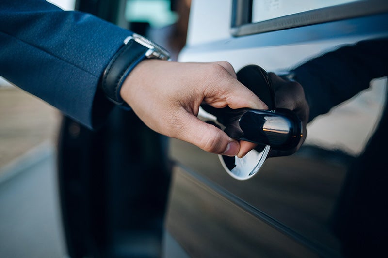Close-up of a hand opening the door handle of a dark-colored car